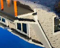 On Cedar Shore Road near the center of Ellison Bay, Wisconsin, the Bayside Resort casts a rippled reflection in a street pool. After a summer shower has moved across the bay, the street can be speckled with small pools of fresh water, perfect mirrors in the crisp sunlight. This photographed reflection gives to the Bayside's building the watery character of Green Bay itself. The shimmer adds a whimsical quality befitting the peninsula where tourists come to play in the exquisite summer weather.